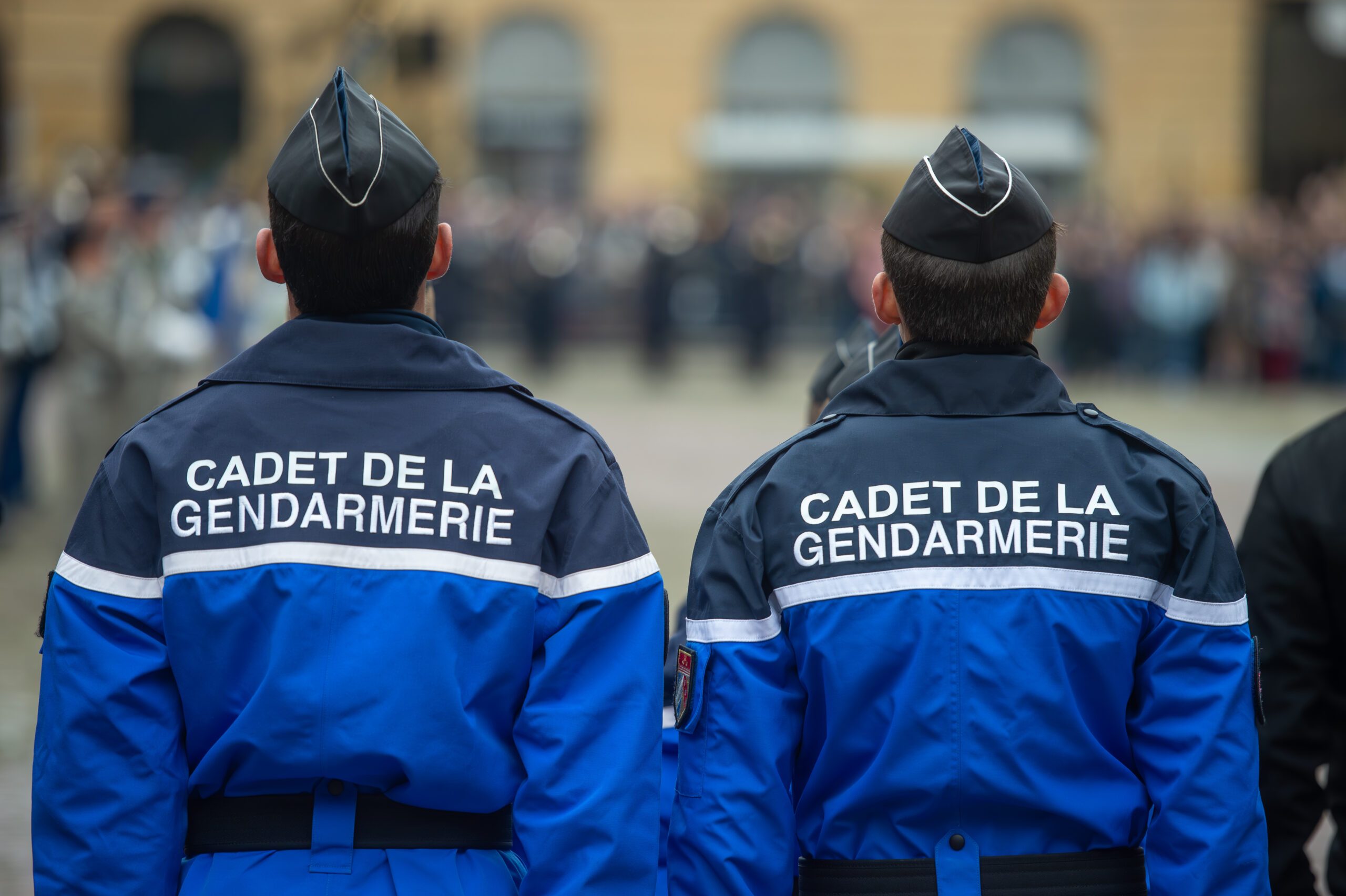 Deux cadets de la gendarmerie en uniforme bleu vus de dos lors d’une cérémonie.