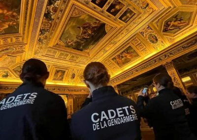 Des cadets de la gendarmerie vus de dos lors d’une visite dans une salle historique au plafond décoré.